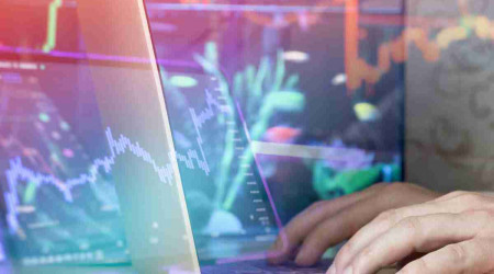 Mano soltando monedas frente a gráfico bursátil simbolizando el primer paso hacia invertir en ETF.